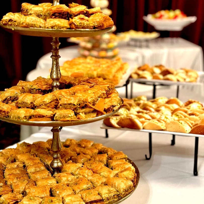 A three-tiered stand overflows with golden baklava, with other Middle Eastern pastries on tables nearby.