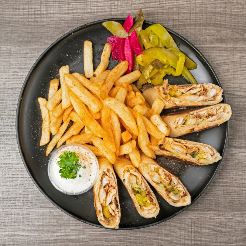 SK Shawarma plate with chicken shawarma wraps, seasoned fries, pickles, and garlic sauce.