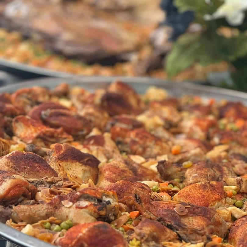 Close-up of a large platter of Middle Eastern chicken and rice, garnished with nuts and vegetables.