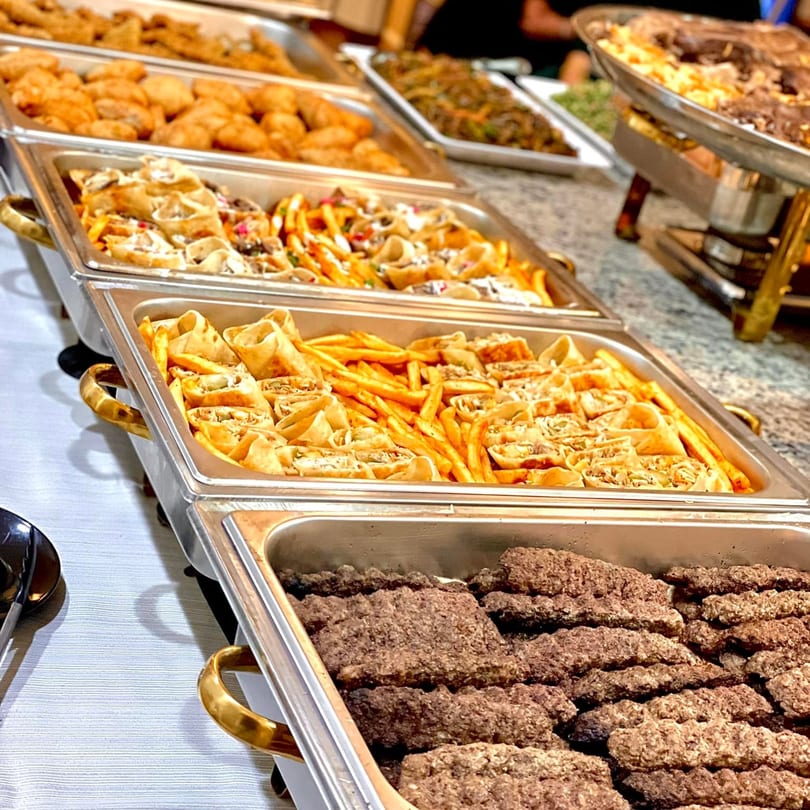 A buffet spread of Middle Eastern dishes, including shawarma wraps, fries, and kofta in chafing dishes.