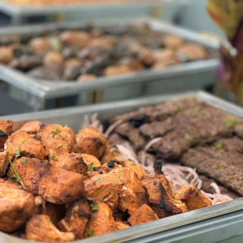 Close-up of two metal trays filled with grilled chicken pieces and ground meat kebabs.