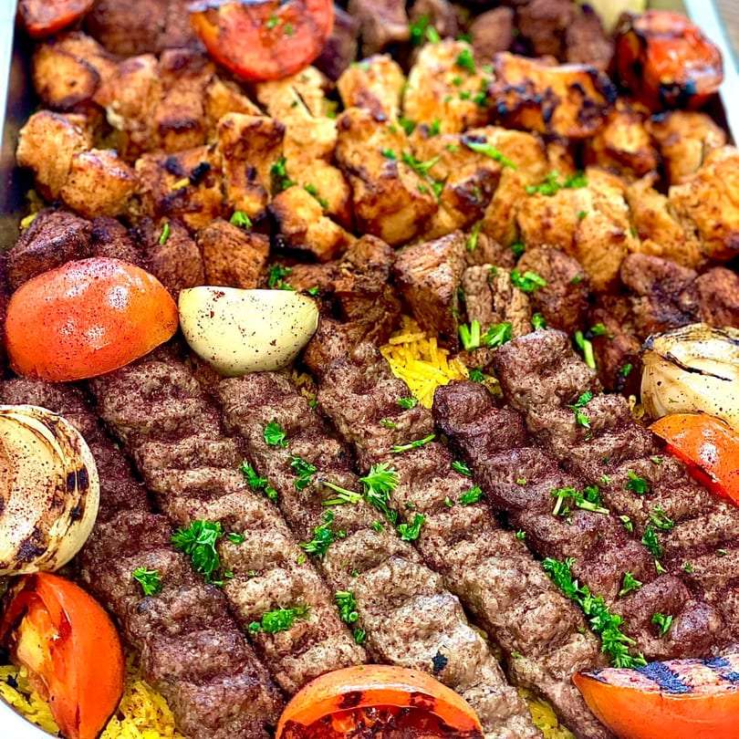 A large platter of grilled chicken, beef kebabs, and kofta, with roasted tomatoes and onions.